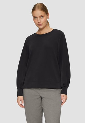 Zwarte lange mouwen sweatshirt met een ronde hals, voorzien van losse mouwen en een geribbelde zoom, gecombineerd met lichtgrijze broeken.