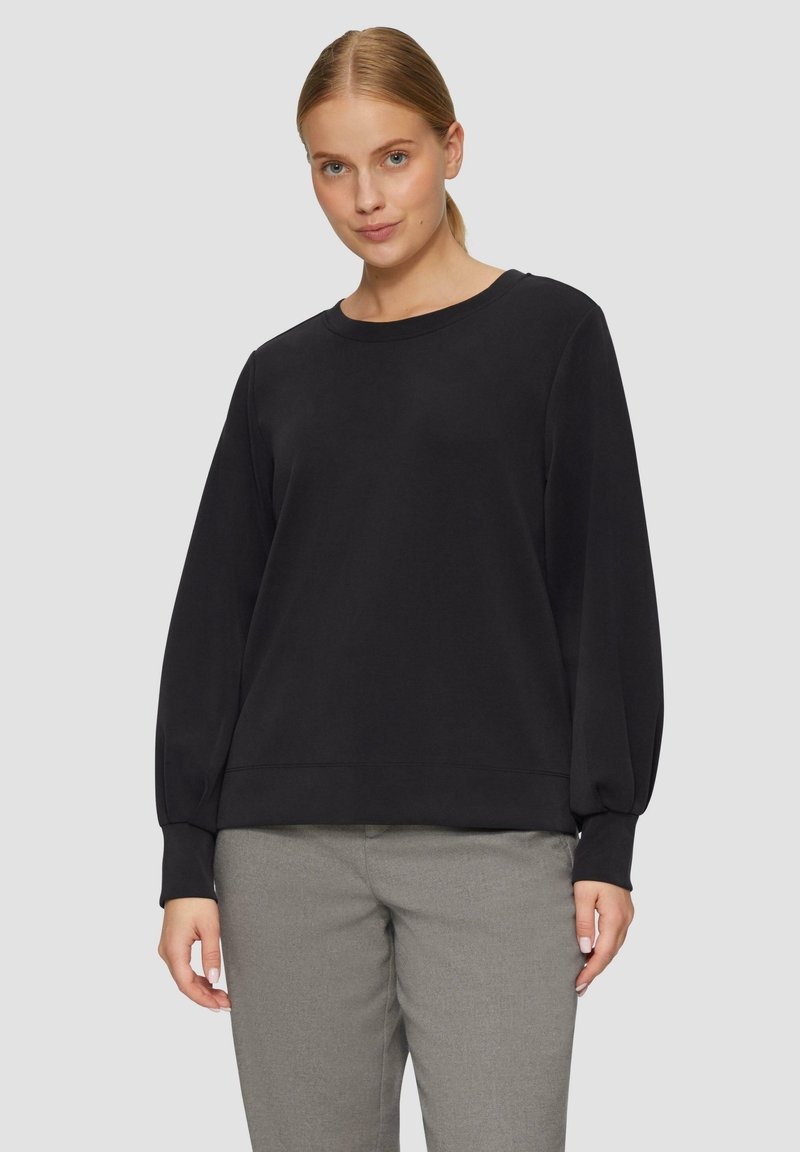 Zwarte lange mouwen sweatshirt met een ronde hals, voorzien van losse mouwen en een geribbelde zoom, gecombineerd met lichtgrijze broeken.