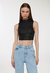 Czarny, krótki bezrękawnik o wysokim dekolcie, z błyszczącą teksturą, w zestawie z jasnoniebieskimi spodniami typu high-waist.