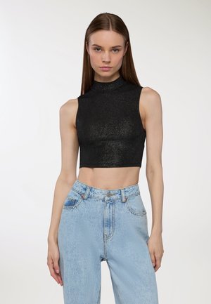 Top nero corto senza maniche con colletto alto, caratterizzato da una texture scintillante, abbinato a jeans a vita alta di colore blu chiaro.