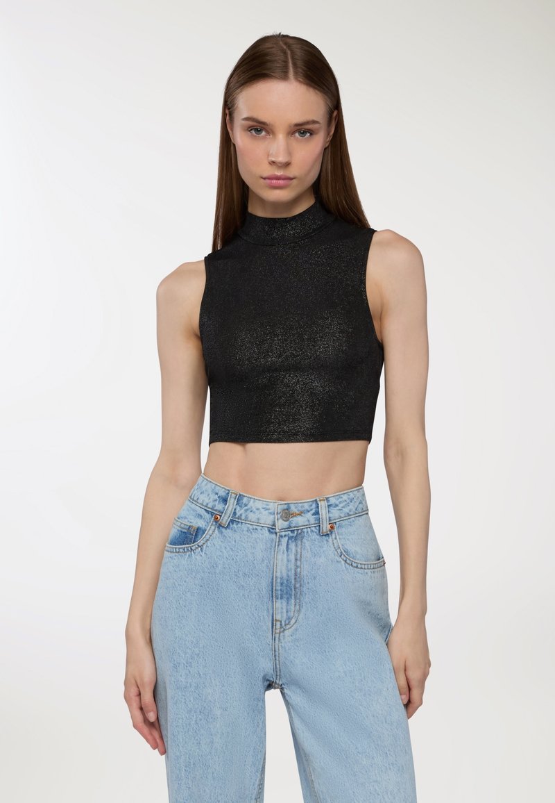 Czarny, krótki bezrękawnik o wysokim dekolcie, z błyszczącą teksturą, w zestawie z jasnoniebieskimi spodniami typu high-waist.