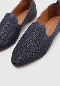 Zapatos de lona azul marino sin cordones con un patrón geométrico texturizado, que presentan un perfil bajo y un interior de cuero suave. Suela marrón.