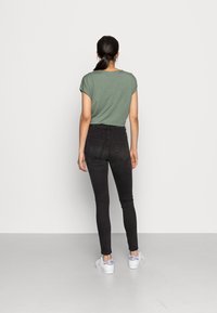 Camiseta verde de manga corta, combinada con jeans skinny negros de tiro alto y zapatillas blancas con un acento colorido en el talón.