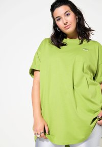 Grøn oversized t-shirt lavet af bomuld med rund halsudskæring og opkrøllede ærmer. Har et lille logo på brystet. Glat tekstur.