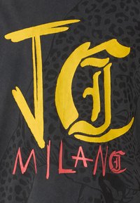 Grafický design s odvážným žlutým textem "JC" a "MILANO" na černém pozadí, s jemně vkombinovaným leopardím vzorem.