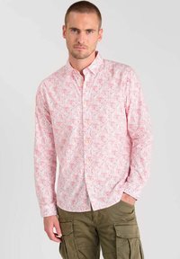 Chemise boutonnière rose clair à motif floral, manches longues et col classique, associée à un pantalon cargo kaki.