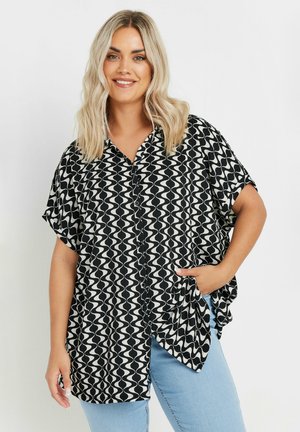 Camicia a maniche corte bianca e nera con motivo a onde, colletto, chiusura con bottoni e vestibilità rilassata, abbinata a jeans azzurri chiari.