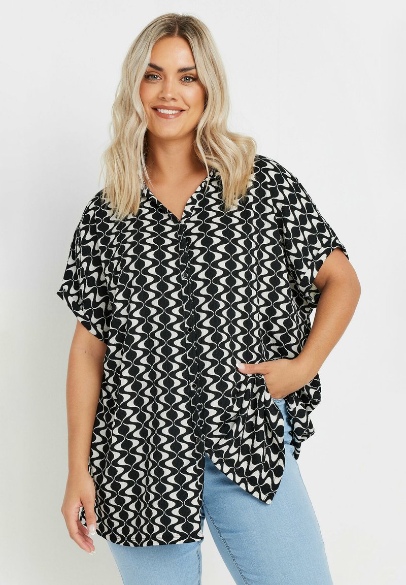 Camicia a maniche corte bianca e nera con motivo a onde, colletto, chiusura con bottoni e vestibilità rilassata, abbinata a jeans azzurri chiari.