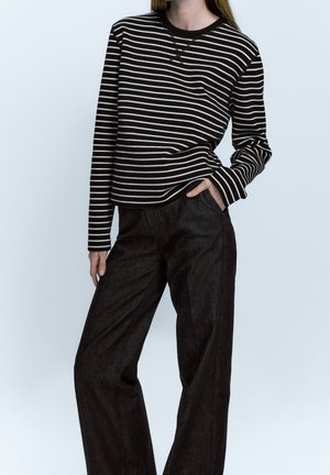 Person wearing a black-and-white striped long-sleeve top and high-waisted, wide-leg black pants with one hand in pocket.