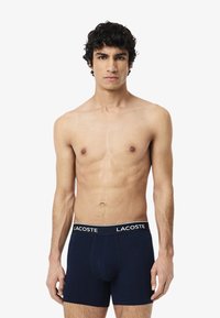 Námornícke modré pánske boxerky s bielym logom Lacoste na páske, vyrobené z mäkkého, elastického materiálu. Strih priliehajúci na telo.