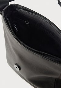 Μαύρη δερμάτινη τσάντα με υφή στην επιφάνεια. Η εσωτερική επένδυση είναι από σκούρο ύφασμα και διαθέτει τσεπάκι με φερμουάρ. Περιλαμβάνει κλείσιμο με μαγνητικό κουμπί.