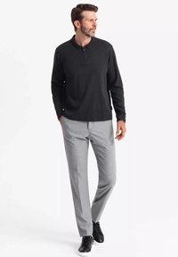 Schwarzes Langarm-Polo mit Reißverschlusskragen, kombiniert mit hellgrauen, maßgeschneiderten Hosen und schwarzen Sneakers. Glatte Textur, moderner Schnitt.