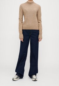 Maglione a coste beige con collo alto, abbinato a jeans a gamba larga blu scuro e sneakers multicolori. Design semplice con una vestibilità comoda.