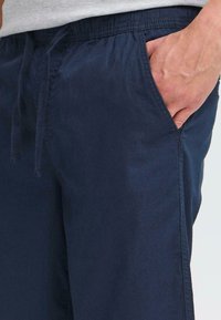 Pantalons en tissu léger bleu marine avec une taille élastique, un cordon de serrage et des poches latérales. Texture lisse avec un design à coupe décontractée.