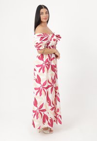 Robe maxi avec un design dénudé d'épaules, motif floral en rose et crème, taille cintrée et tissu fluide. Caractérisée par un matériau léger.