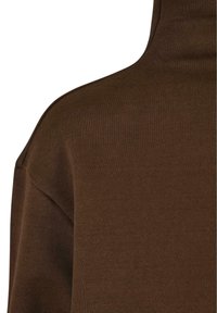 Gros plan d'un pull en maille marron à manches longues montrant l'épaule et la partie supérieure de la poitrine avec un col montant.