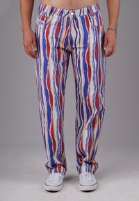 Gestreifte Baumwollhose mit vertikalen Mustern in Rot, Blau und Weiß, entspannter Schnitt und Fronttaschen. Weiße Sneakers getragen.