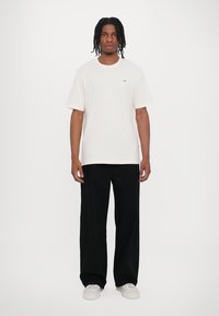 Witte katoenen T-shirt met een ronde hals, korte mouwen en een klein logo. Gepaard met losse zwarte broeken en witte sneakers.