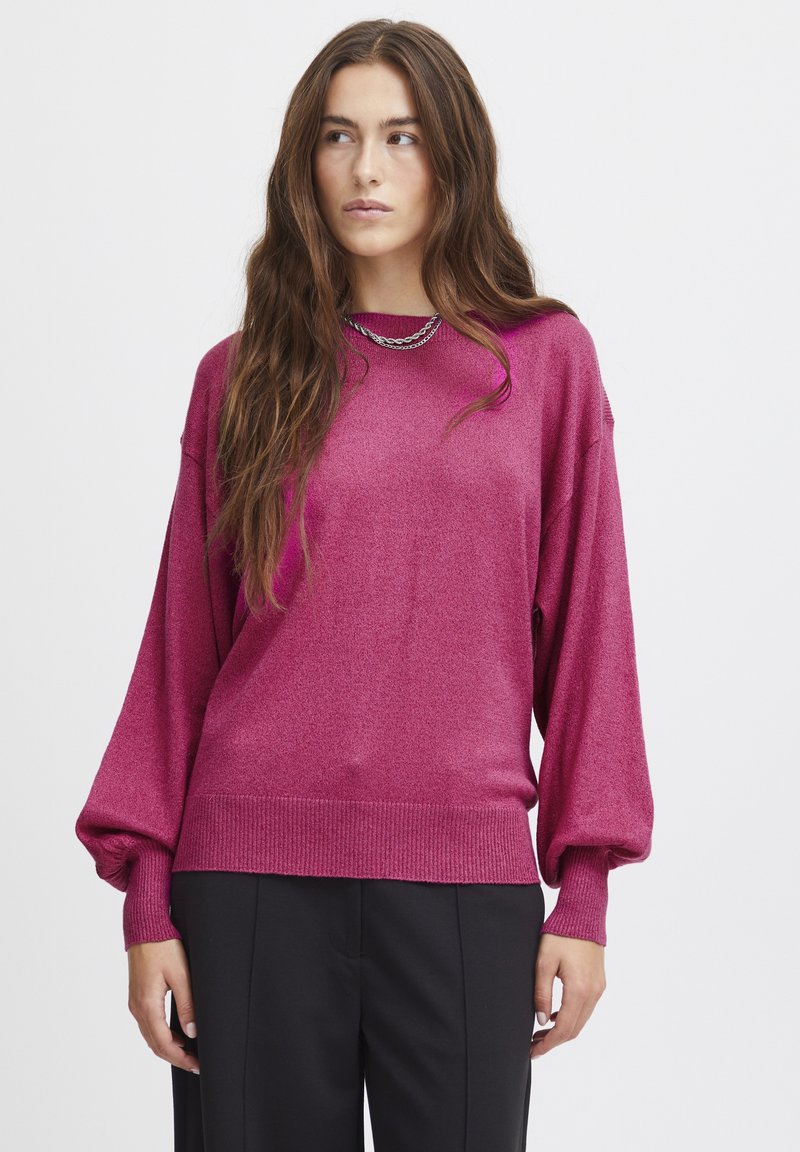 Maglione oversize magenta realizzato in un morbido tessuto lucido, con orlo a coste e maniche a palloncino, abbinato a pantaloni neri.