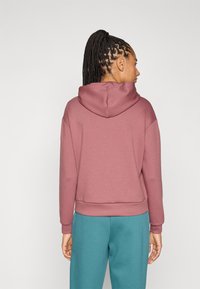 Φούτερ με κουκούλα σε ανοιχτό ροζ χρώμα, με ριμπ τελείωμα, τσέπη καγκουρό και άνετη εφαρμογή, συνδυασμένο με τζόγκερ παντελόνια σε τιρκουάζ χρώμα.