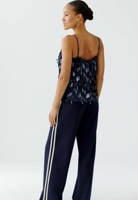 Marineblaues Tanktop mit geschichteten Pailletten, verstellbaren Trägern, kombiniert mit marineblauen weiten Hosen mit cremefarbenen Seitenstreifen. Glatte Textur.