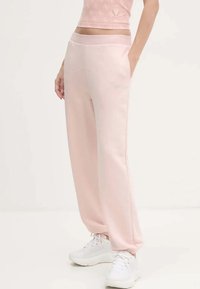 Roze joggingbroek gemaakt van zacht materiaal, met zijzakken, een relaxte pasvorm en subtiele versieringen voor extra detail.