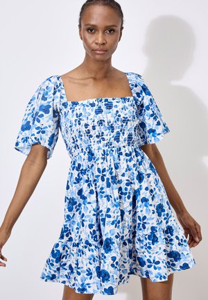 Blaues Blumenkleid mit Puffärmeln, gerafftem Oberteil und gestaffeltem Rock. Aus leichtem Stoff gefertigt; hat einen quadratischen Ausschnitt.