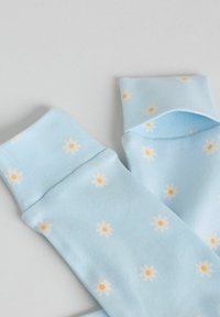 Chaussettes bleu clair avec de petits motifs de marguerites blanches et jaunes, posées à plat sur une surface claire.