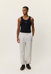 Μαύρο αμάνικο τοπάκι με λογότυπο, συνδυασμένο με ανοιχτό γκρι φόρμα με ελαστικές μανσέτες και μικρό λογότυπο, φορεμένο με μαύρα παπούτσια.