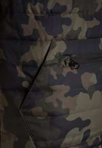 Sekcja kurtki puchowej z kamuflażem, z pikowaną fakturą, w ciemnozielone, brązowe i czarne wzory, z dyskretną kieszenią na zamek.
