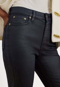 Melnas džinsa bikses ar šauru piegriezumu, ar zelta aksesuāriem, piecām kabatām un teksturētu audumu. Klasiska jostasvietas daļa ar jostu cilpām.