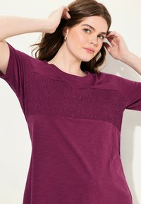 Camiseta burdeos de manga corta, con una banda texturizada en el pecho, fabricada en un tejido suave y ligero. Ajuste suave al cuerpo.