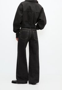 Jean noir à jambes larges et sweat-shirt oversize sombre avec un ourlet court, présentant des poignets côtelés et une finition texturée.