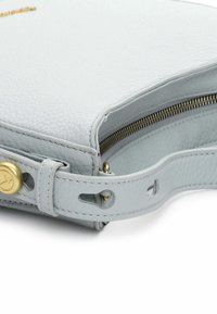 Jasnoszara skórzana torebka o teksturowanej powierzchni, wyposażona w złoty zamek błyskawiczny, złoty ozdobny guzik oraz odpinany pasek z wyciętymi detalami.