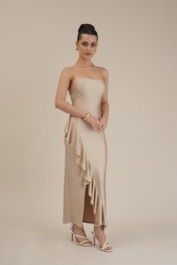 Beige satin midi-kjole med en tettsittende bodice, asymmetrisk volangdetaljering på siden og høyt splitt. Kombinert med hvite høye sandaler.
