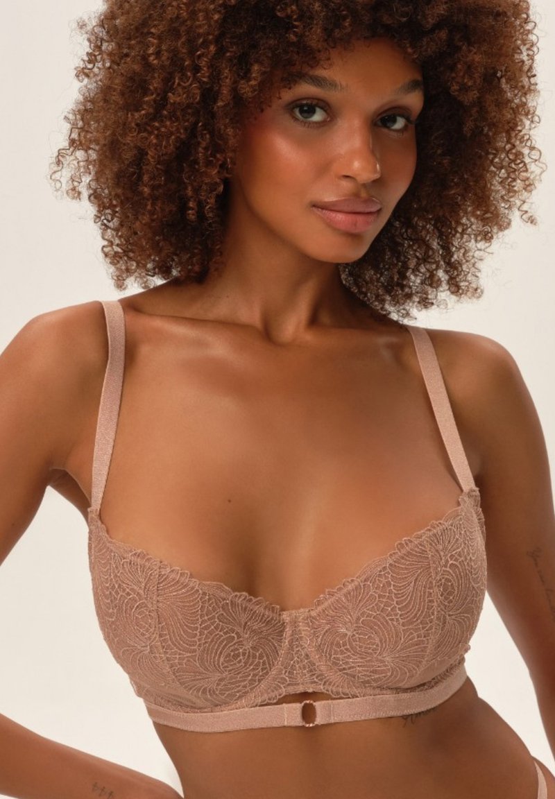 Koronkowy stanik w miękkim odcieniu nude z kwiatowym haftem, wsparciem w postaci drucików, regulowanymi ramiączkami oraz centralnym akcentem w postaci guzika.