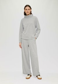 Lichtgrijze, lange mouwen pullover met een hoge kraag, gecombineerd met brede grijze sweatpants. De outfit heeft een casual, zachte textuur.