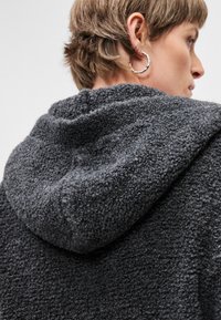 Felpa con cappuccio grigio scuro e texture, realizzata in un materiale morbido e peloso, dotata di un grande cappuccio e dettagli di cucitura ben visibili.