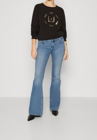 Czarna bluza z okrągłym nadrukiem z metalicznymi akcentami "LJ". Jasnoniebieskie dzwony dżinsowe z dopasowanym stanem i delikatnym przetarciem. Czarne szpiczaste buty.