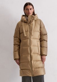 Bežs pūkains mētelis ar kapuci, ar priekšējo rāvējslēdzēju, izšūtu tekstūru, regulējamiem siksnām un sānu kabatām. Gluda, spīdīga auduma.