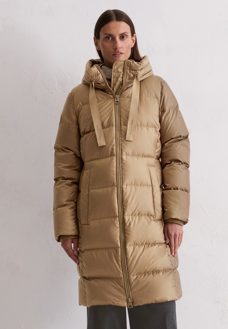 Bežs pūkains mētelis ar kapuci, ar priekšējo rāvējslēdzēju, izšūtu tekstūru, regulējamiem siksnām un sānu kabatām. Gluda, spīdīga auduma.