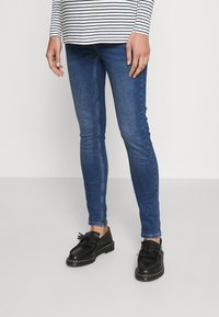 Tunna blå denimjeans med en slät yta, tillsammans med svarta läderskor med fransdetaljer och tjock sula. Randig långärmad tröja.