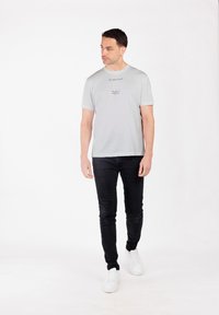 Camiseta gris claro de manga corta y cuello redondo, con diseños de texto en la parte delantera, combinada con jeans negros ajustados y zapatillas blancas.