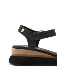 Sandalia de ante negra con una correa ancha, acento de herrajes dorados, plataforma de capas en colores negro, beige y marrón. Suela texturizada para mayor agarre.