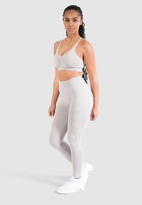 Atletiskt set bestående av en ljusgrå, kort sport-bh med rynkdetalj och höga, tajta leggings, båda i ett mjukt och stretchigt tyg.