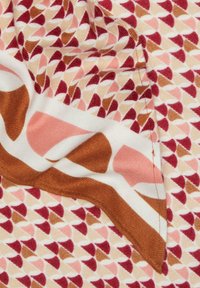 Tissu à motifs présentant de petites formes triangulaires en rouge, rose et marron sur un fond crème. Texture lisse avec des accents contrastants.