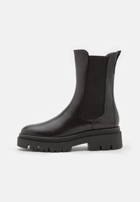 Bottines noires en cuir avec des panneaux latéraux élastiques et une semelle en caoutchouc épaisse et texturée. Fini lisse, bout arrondi et détails de couture contrastants.