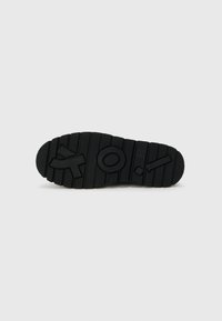 Talpa de cauciuc negru cu caneluri adânci, logo central ridicat și detalii punctate. Dispune de un design plat și robust pentru tracțiune.