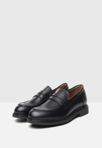 Mocasines de cuero negro con un acabado suave, que presentan costuras decorativas y una punta afilada. Tacón bajo y diseño sencillo de poner y quitar.