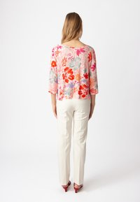 Blusa con stampa floreale rosa, dotata di maniche 3/4 e scollatura arrotondata. Abbinata a pantaloni color crema e tacchi rossi.